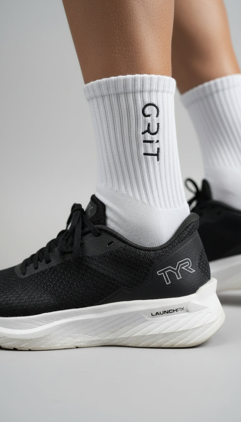 Black running shoe with white sole and 'TYR' branding, worn with a white sock displaying 'GRIT'.