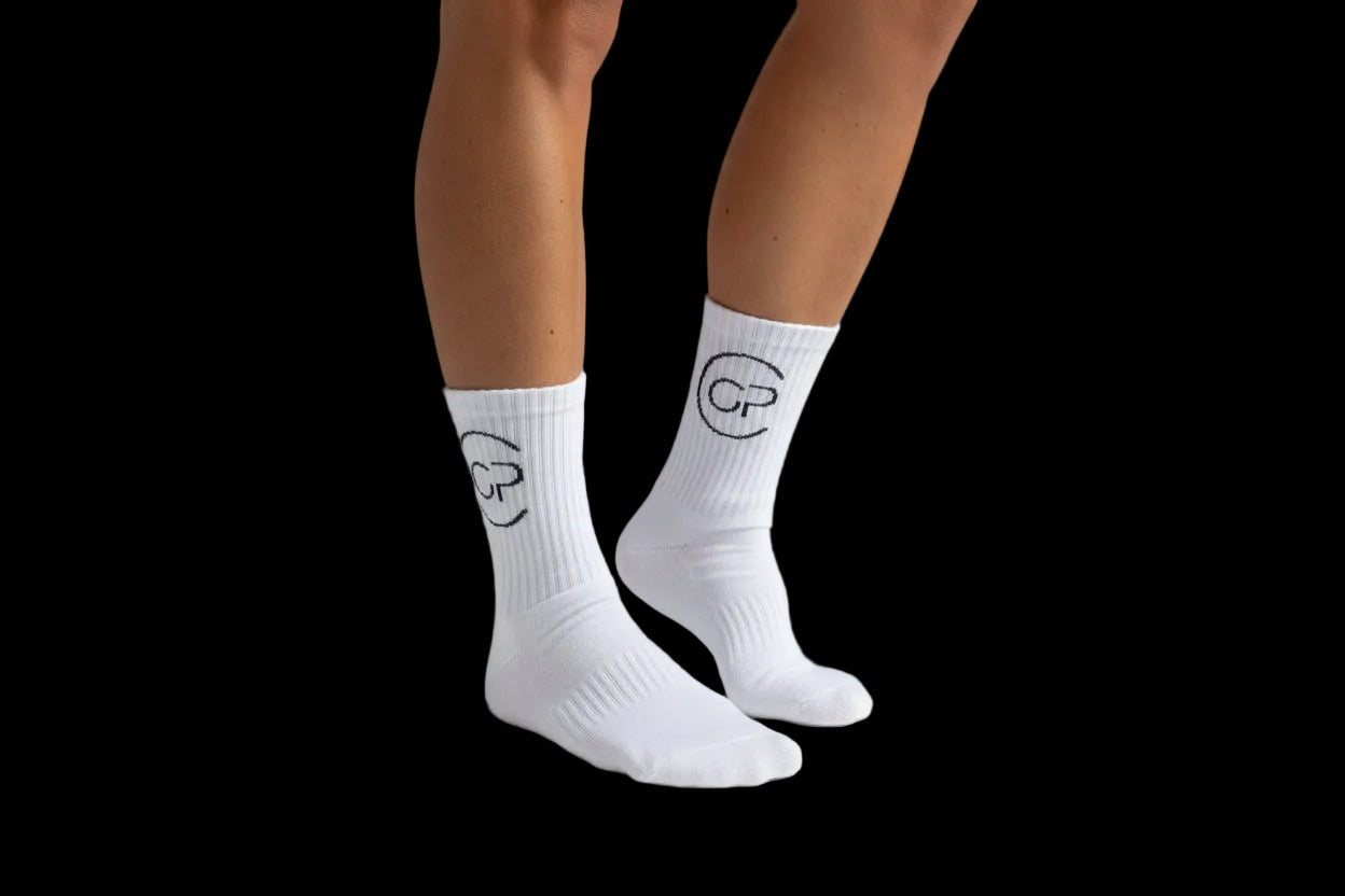 White socks with black logo worn by a person on a carpeted floor.