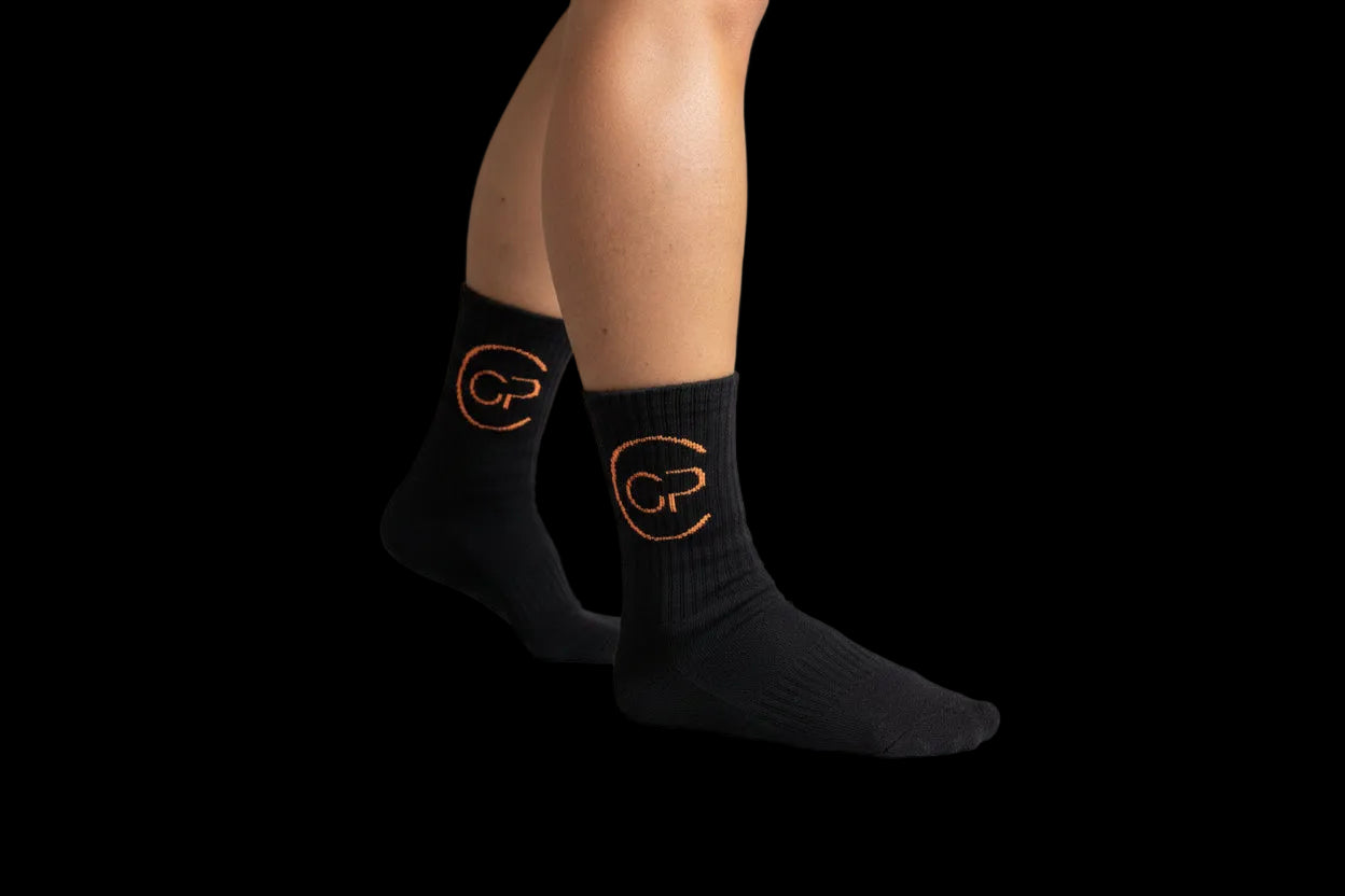 Person wearing black socks with orange designs on a textured wall background